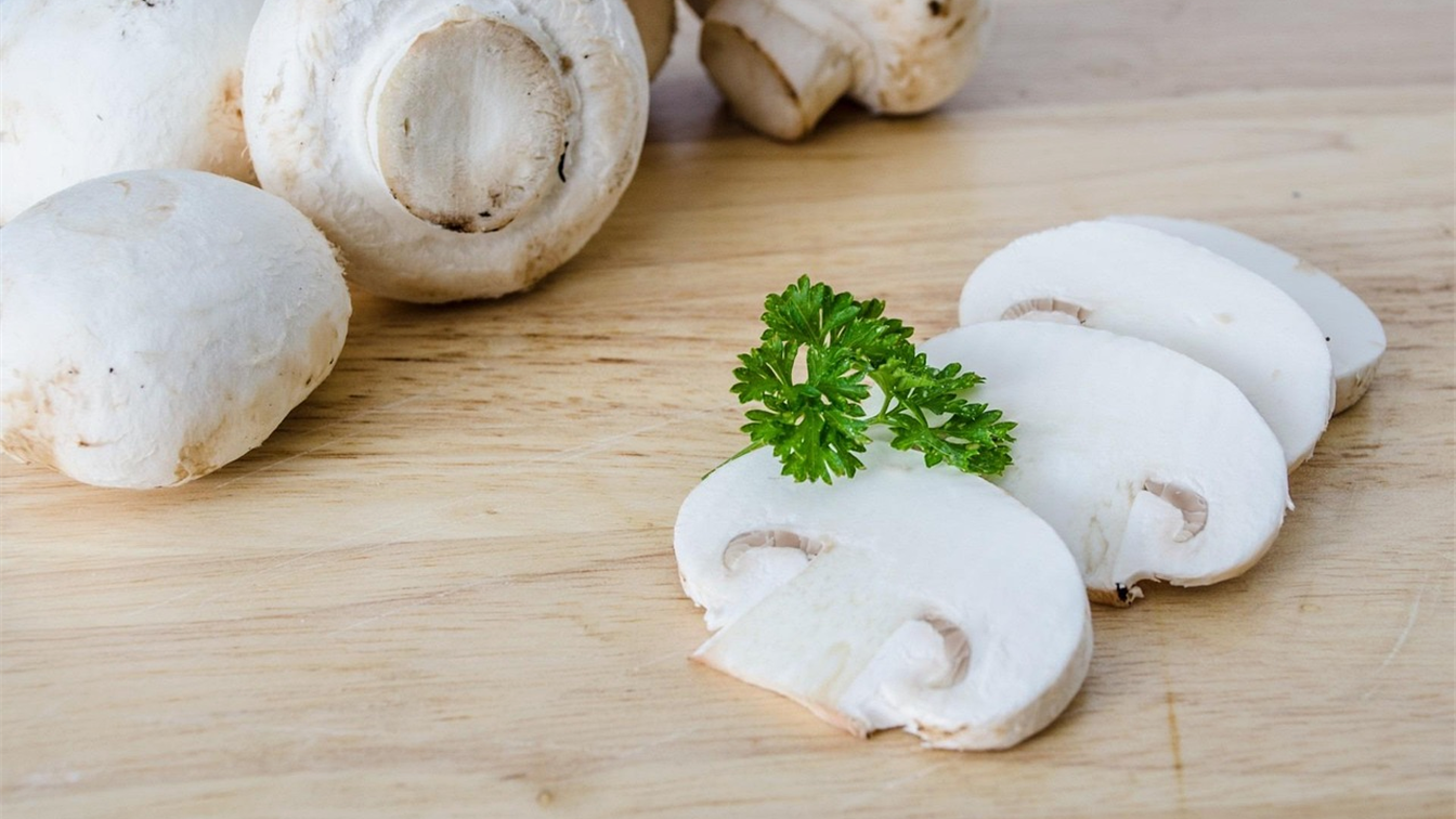 Cogumelos champignon frescos inteiros e fatiados sobre tabua de madeira