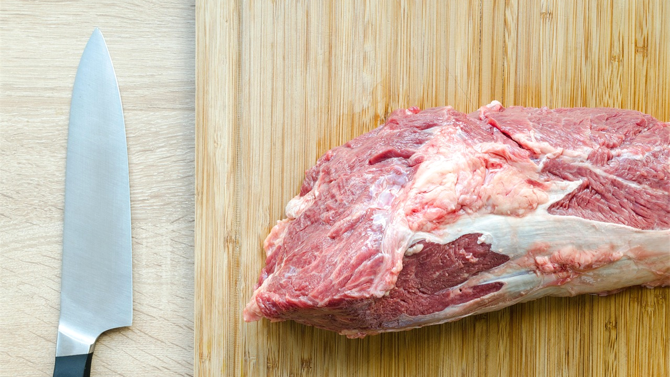 Peça de carne bovina crua sobre tábua de madeira ao lado de uma faca