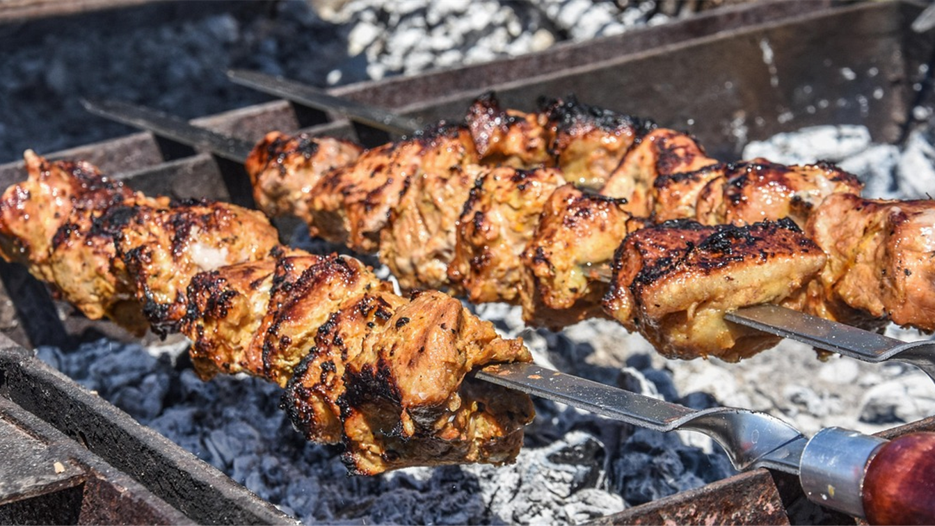Espetinhos de carne grelhando sobre brasas em churrasqueira